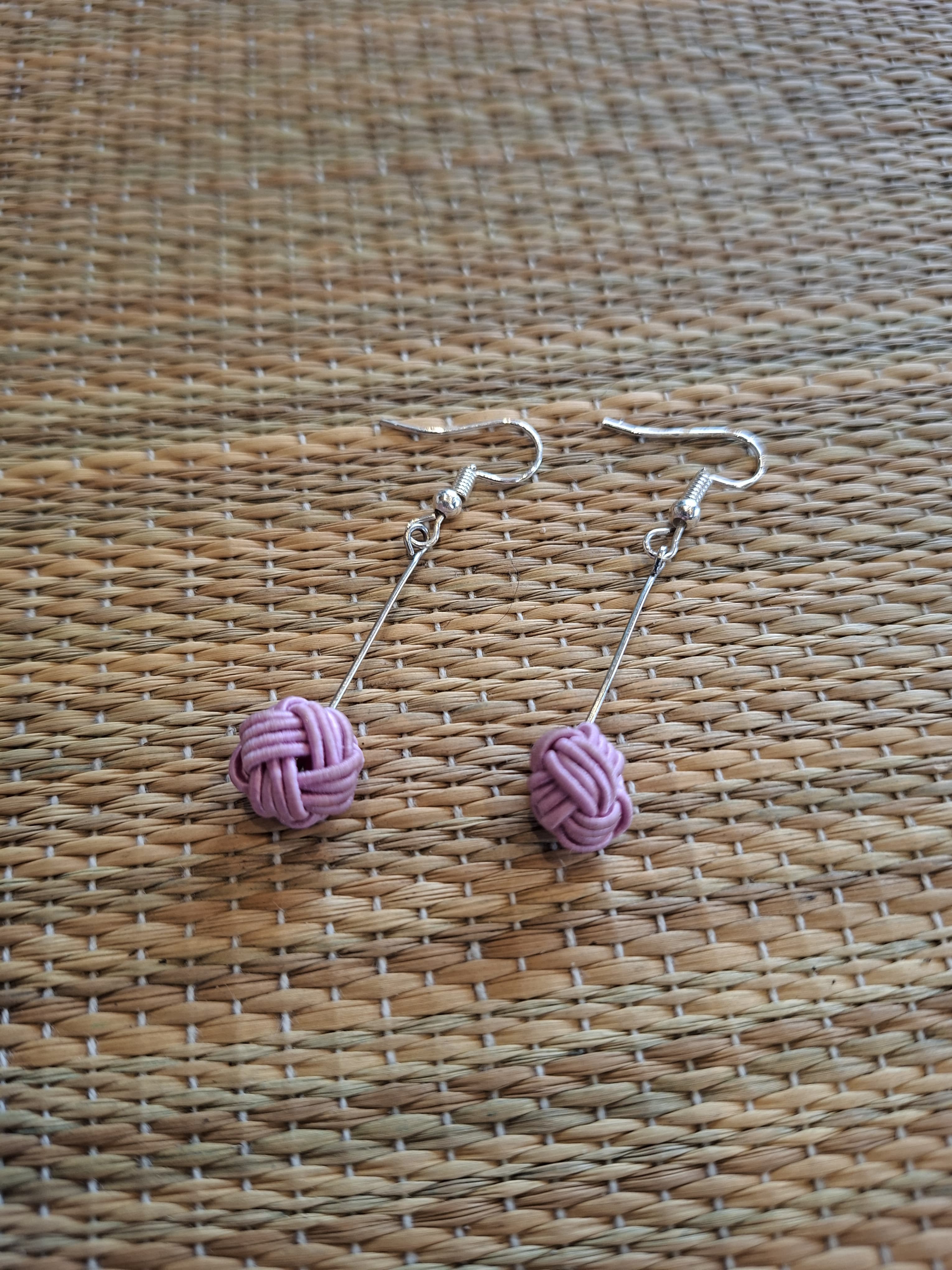 Pink mizuhiki knotted cord earrings on a woven background